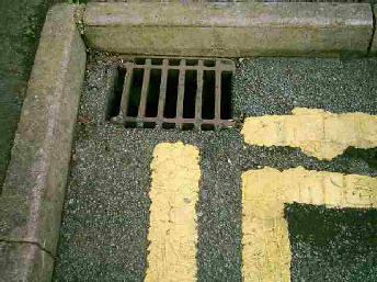 Corner of a road with a drain and yellow road lines