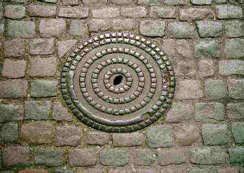 A manhole cover with a cobble like design set in a cobbled street